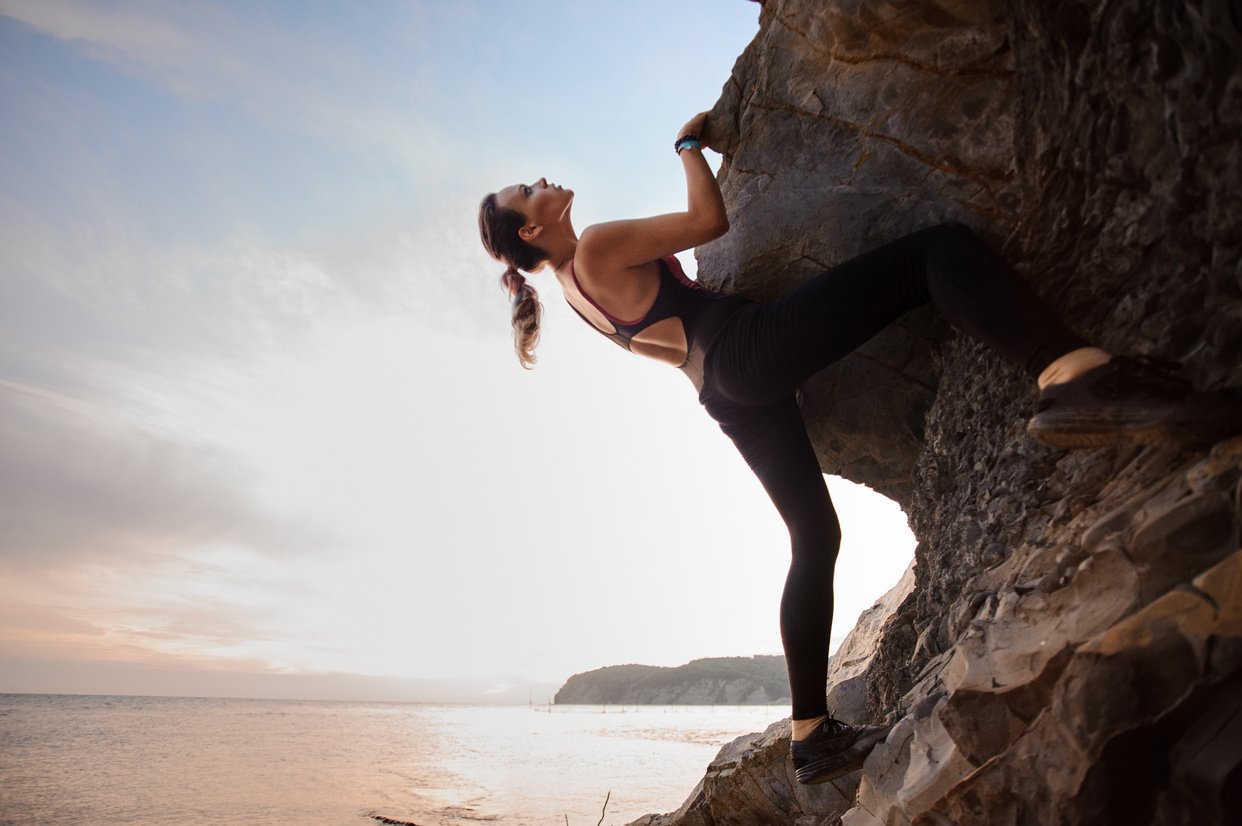 Young female rock climber climbing challenging route on overhanging cliff